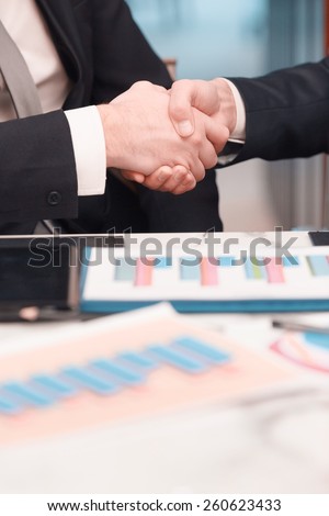 Businessmen handshaking. Cropped image of two confident business men handshaking and smiling while sitting at the table together with their colleagues