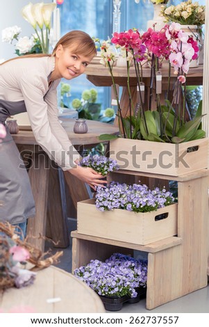 Look at this wonder. Female owner of a flower shop holding flower pot and looking at the camera