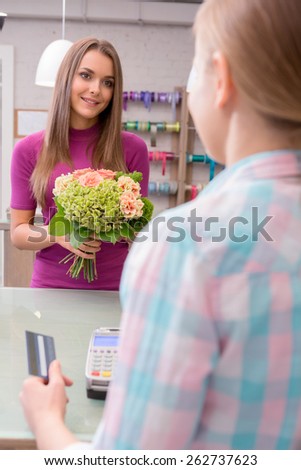 This is a special gift to a special person. Selective focus of a beautiful woman with a floral bouquet while a florist holds a credit card and card reader to make a payment