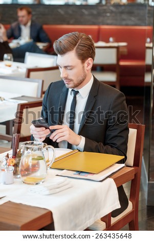 Need to answer. Vertical view on the young attractive business manager looking at his phone during business lunch with colleagues