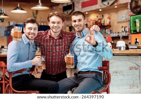 Meeting with best friends. Cheerful young men in casual wear holding glasses with beer and smiling in the pub