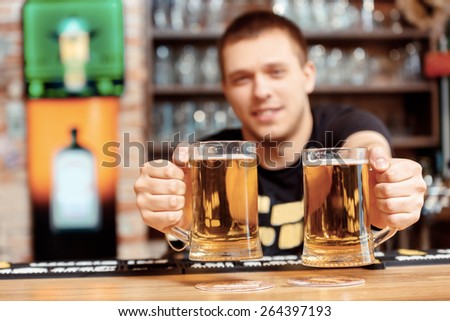 Freshly tapped beer. Selective focus on close up of glasses with beer which cheerful young bartender stretches out and smiles