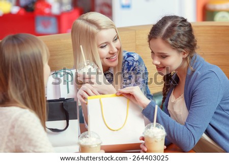 Just have a look at this wonder. Happy young girls look inside the shopping bag with excitement and discussing their purchases by the cocktail