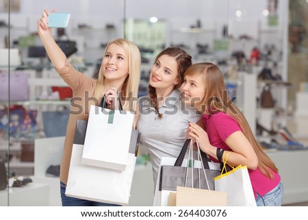 Smiley and cheerful shoppers.  Beautiful and young girl teenagers in casual clothes holding bags and making selfie in the shopping mall
