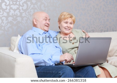 Elderly couple using a laptop computer as they sit side by side on a couch sharing the internet
