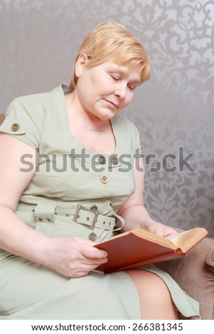 World of fiction. Elderly woman relaxing at home reading a book in her living room