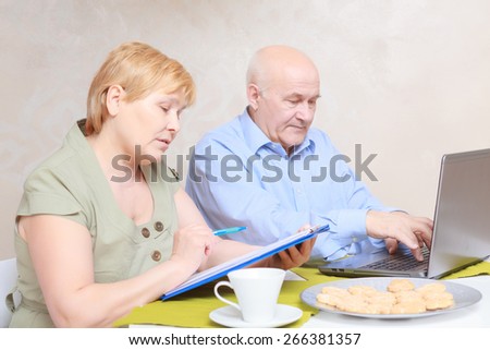 Family business.  Elderly couple busy with making notes and printing text on a laptop at home