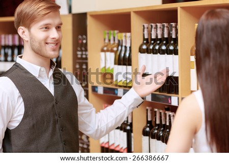 Excellent choice. Close-up of a salesman giving young woman advice on buying bottle of wine