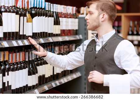 Store audit. Young handsome salesman in a liquor store examining rows of wine bottles