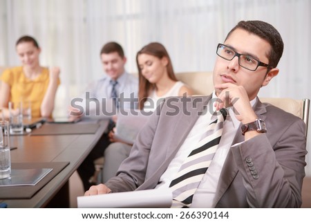 Thinking over next steps. Handsome concentrated business manager touching his chin with hand thinking over information at the meeting