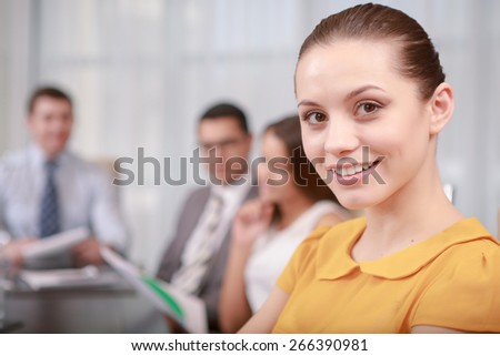 Effective business partnership. Close-up of a pretty young business manager at the business meeting smiling at a camera while her partners sitting in a row at the table