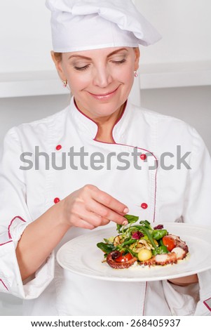 Beautiful mature female cook holding a plate and serving octopus salad with mash-salad