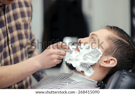 Shaving the beard. Barber putting some shaving cream on a client before shaving his beard in a barber shop