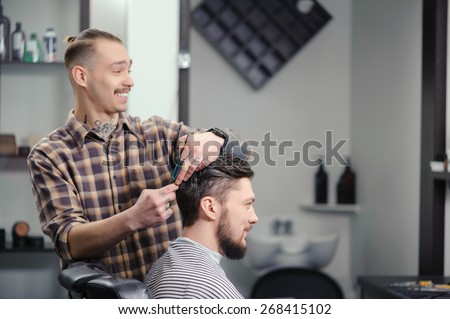 Joyful conversation. Cheerful skillful barber making a haircut with scissors to a young bearded man