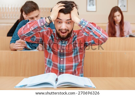 Get crazy. Young emotional students grabs his head and screams looking at a book in class