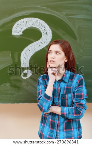 Mystery. Young thoughtful student thinking on some question with a question mark on a chalkboard on the background