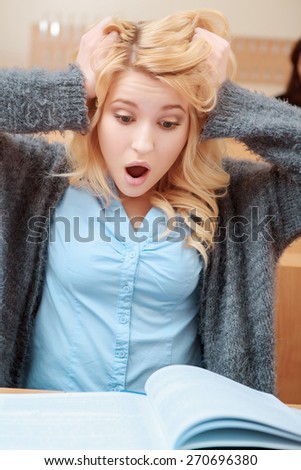 Oh my God. Young beautiful blond female student grabs her head looking with surprise and astonishment into the exercise book