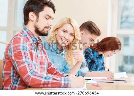 Happy students. Young smiling blond female student showing thumb up sitting with her group mates at the desk