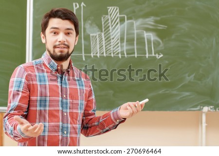 College classes. Young agitated male student standing on the background of a chalkboard with graph on it