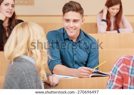 College flirts. Young handsome male student smiling to his peer turning back to him in an auditorium class