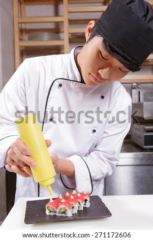 Making a perfect presentation. Young sushi chef pouring a sauce on tuna sushi rolls put on a rectangular black plate