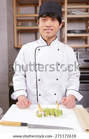 Master chef.  Proud and confident young sushi chef smiling to the camera standing near the table with cooked green rolls
