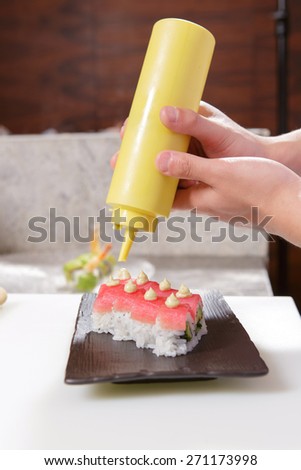 Asian sauce. Closeup on hands of a cook pouring hazel sauce on tuna sushi rolls