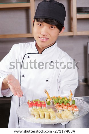 Proud cook. Confident young Asian sushi cook points with hand on a plate with sushi set