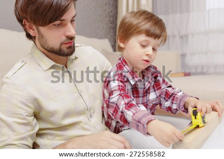 Learning to construct. Close-up of a young father and his smart son applying a ruler in toy wooden constructor