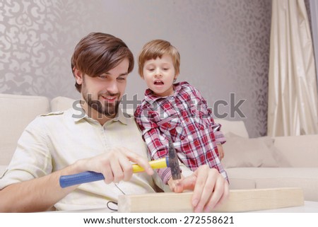 Men power. Young joyful father and curious son applying a hammer in toy constructor