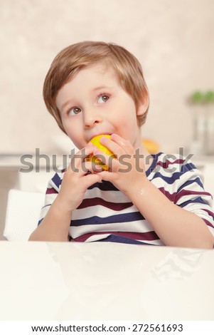 Lemon taste. Small kid biting piece of lemon while preparing home lemonade with his father