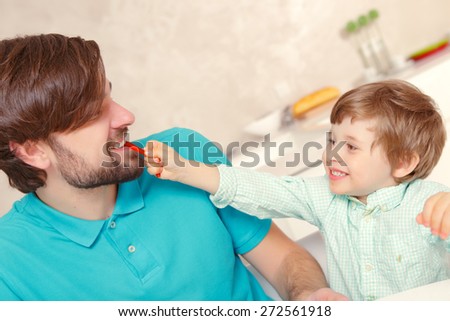 Tastes good. Small boy happily feeding his young father with a slice of pepper at home kitchen