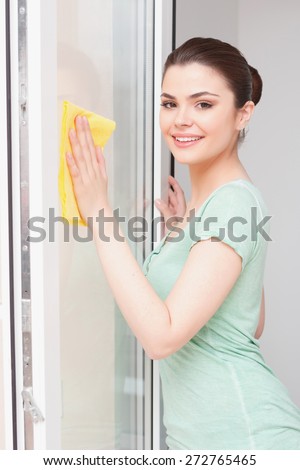 Transparent view. Smiling woman wiping window with help of yellow cloth