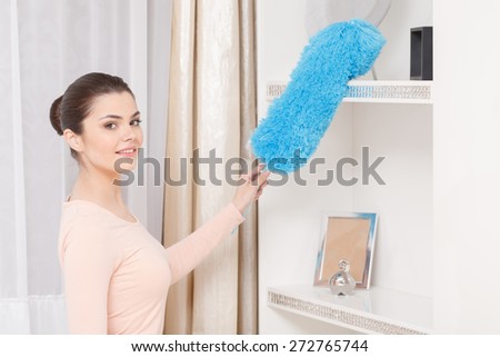 Self-pride. Fancy woman dusting shelf with the help of blue cleaning sweep