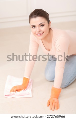 Cleaning sport. Young pretty lady washes floor on her knees with help of white cloth and orange rubber gloves