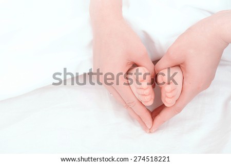 Gentle touch. Woman holding tiny baby feet in her hands like a heart