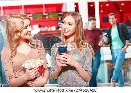 Eye contact. Two girls with cola and popcorn in hall before watching film in cinema and looking at each other.