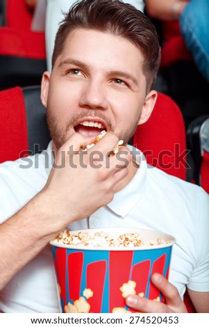 It is all mine. Young man greedy eating popcorn in cinema while watching film.