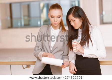 Discussing a plan. Young businesswoman holding a folder and her colleague drinking coffee having a talk