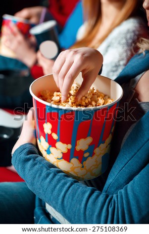 So tasty. Close up of woman taking popcorn out of box in cinema.