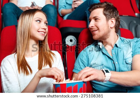 One for two. Two young people sharing popcorn in cinema and looking at each other.