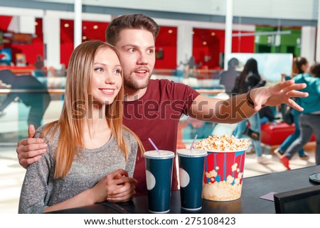 Lets take everything. Youthful man and woman buying popcorn and coke before watching film in cinema.