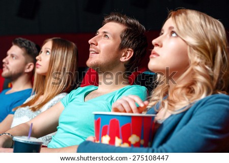 Breath-taking. Pretty blond woman with popcorn in cinema near other viewer.