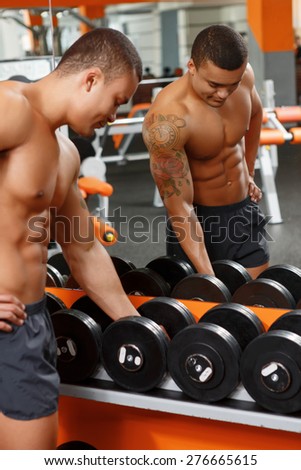 Getting ready. Handsome young muscular man taking one of barbells in front of mirror in gym