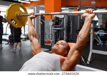 Pushing up.  Lying handsome powerful man lifting barbell in sport gym.