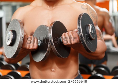 More means better.  Close up of man lifting two dumbbells in sport gym.