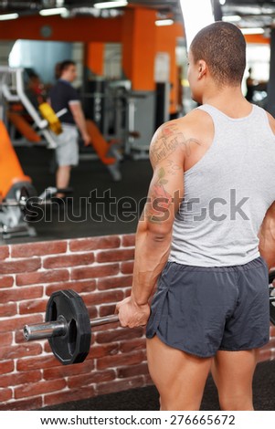 Health and strength. Back view of handsome muscular weightlifter standing in front of mirror in gym