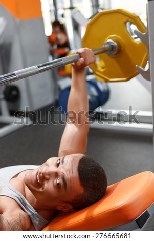 Playing hard. Handsome lying muscular man lifting barbell in sport gym.
