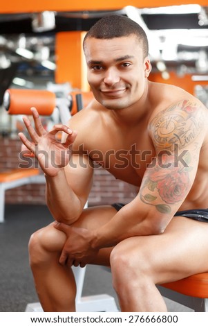 Everything is great. Muscular young man sitting in sport gym and pointing ok.