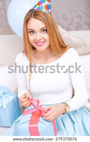 Time to open presents. Young beautiful blond girl wearing cone cap pulling a ribbon to open her birthday gift